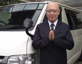 移動火葬車の前で合掌する代表 瀧和治